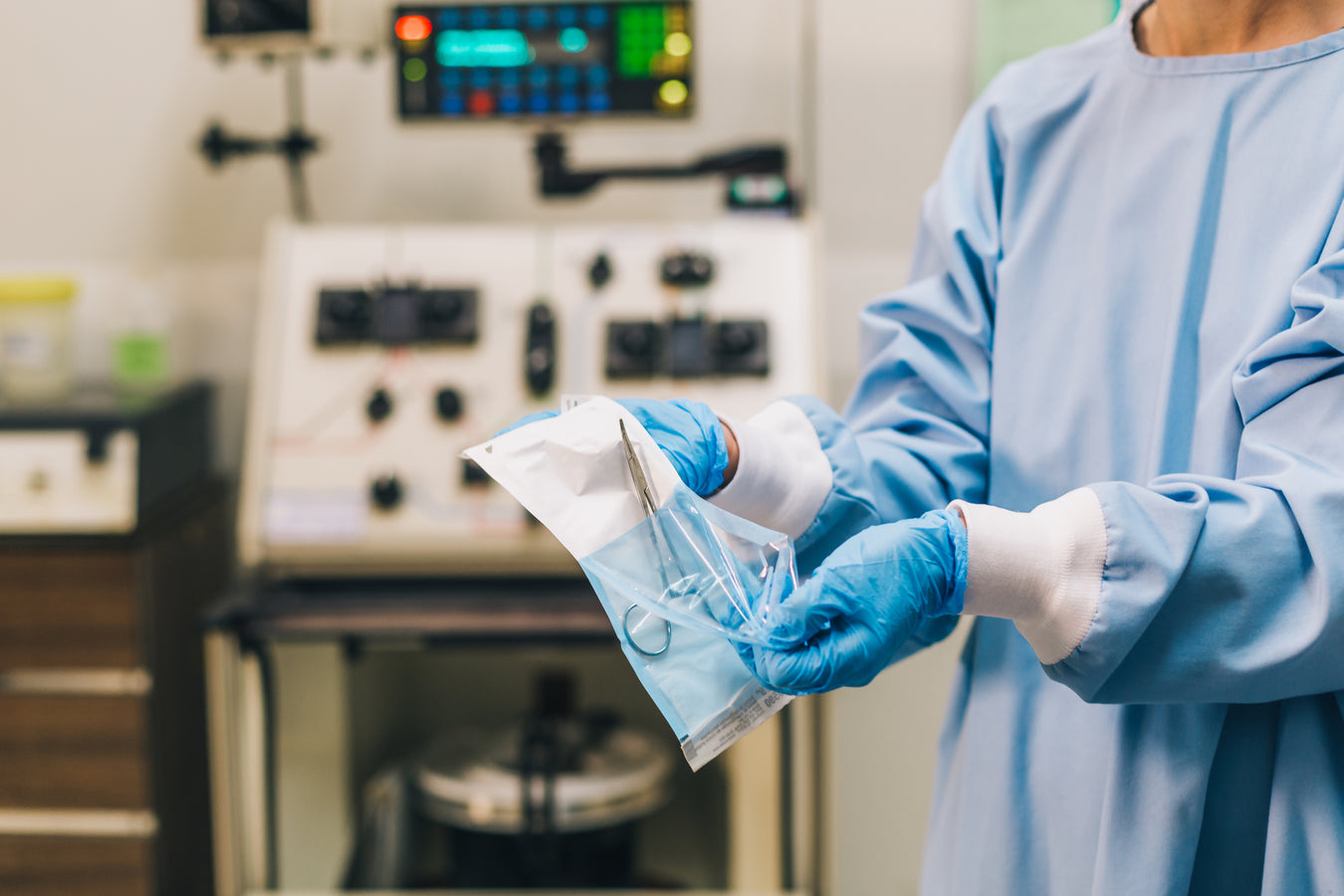 Medical professional in scrubs unwraps sterile forceps